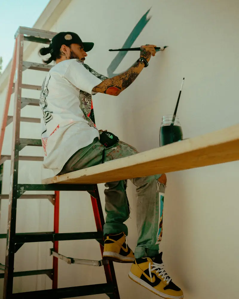 Artisan peintre appliquant de la peinture sur un mur extérieur depuis une échelle