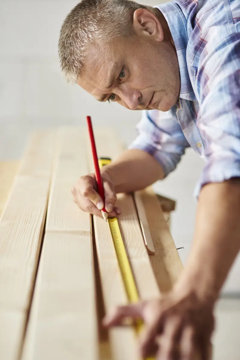 Artisan poseur de parquet mesurant des lames de bois au mètre ruban