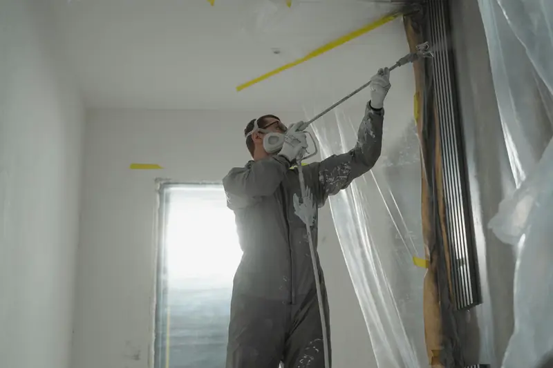 Artisan peintre appliquant de la peinture au plafond en combinaison de protection