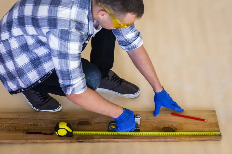 Artisan posant un parquet flottant — mesure des lames au mètre ruban
