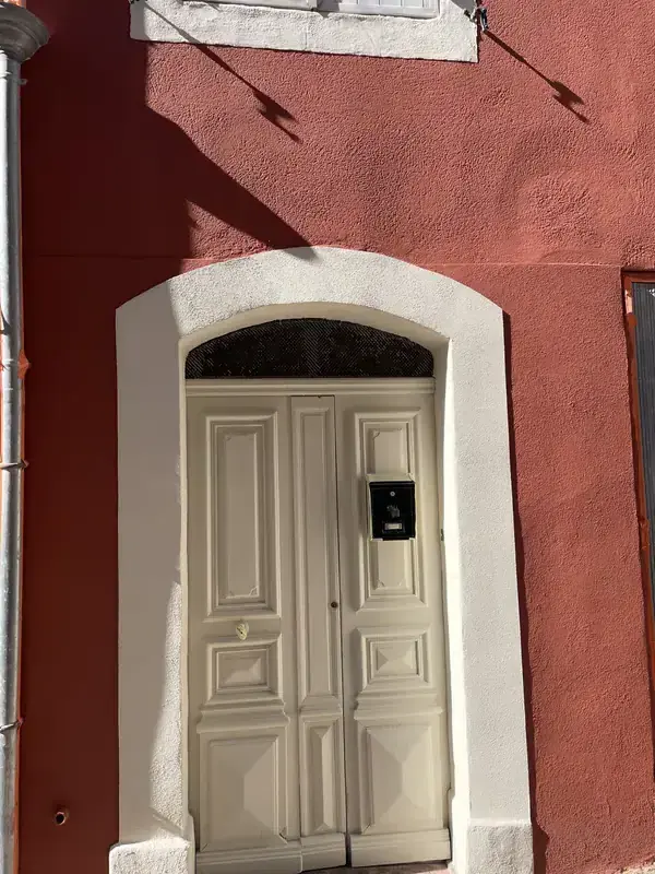 Façade après ravalement à Béziers — enduit taloché rouge, porte repeinte en blanc crème
